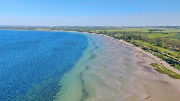 Ein Luftbild einer Küstenregion mit klarem, blauem Wasser, einem Sandstrand und grünen Feldern.