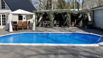 A swimming pool with a covered patio area, a white tent, and outdoor furniture.