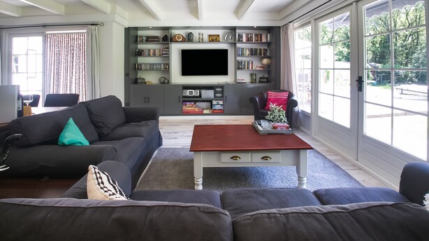 A living room with a large flat-screen TV, dark sofas, a coffee table, and a bookshelf filled with books and decorative items. - Villa in Drents-friese Forest With Pool (Wateren)
