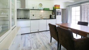 A modern kitchen with white cabinets, a wooden dining table, and a window with curtains. - Villa in Drents-friese Forest With Pool (Wateren)