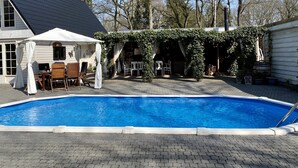 A swimming pool with a covered patio area, outdoor furniture, and a small white building. - Villa in Drents-friese Forest With Pool (Wateren)