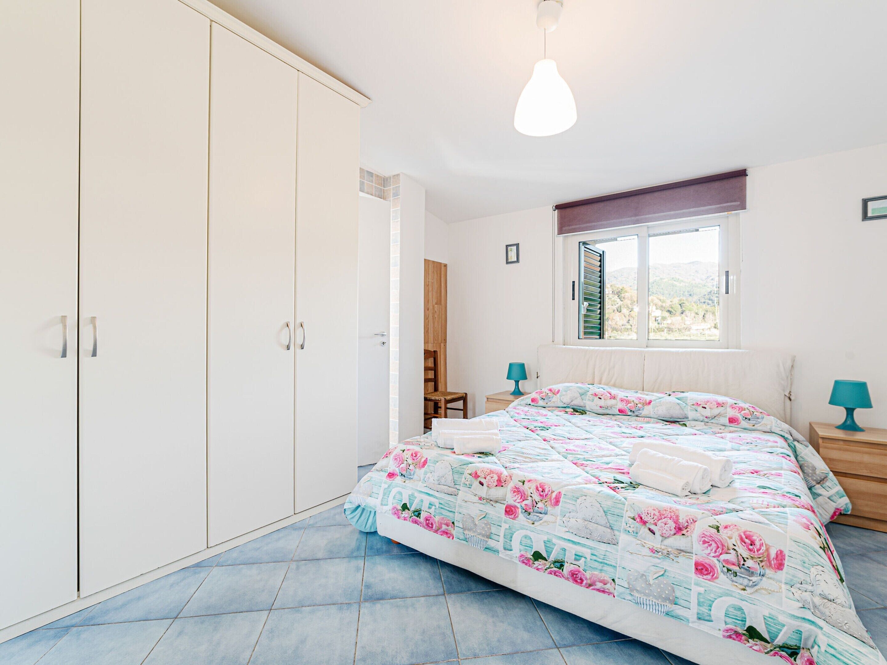 A bedroom with a bed, a wardrobe, a window, and a hanging light fixture.