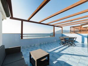 Una terraza en la azotea con una mesa y sillas, un sofá de mimbre y vistas al mar.