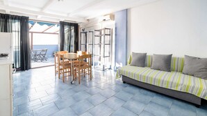 A spacious living area with a sofa, a dining table with chairs, and a view of the sea through large windows. - Belvilla by OYO Apartment in Policastro Bussentino (Santa Marina)