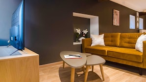 A modern living room with a flat-screen TV, a mustard-colored sofa, a small round table, and a wooden floor. - Superb Duplex Ideally Located in the Centre of Aywaille (Aywaille)