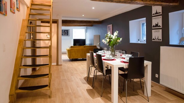 A dining area with a wooden staircase, a dining table set with red and white tableware, and a vase of flowers. - Superb Duplex Ideally Located in the Centre of Aywaille (Aywaille)