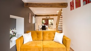 A modern living room with a mustard yellow sofa, wooden beams on the ceiling, and a staircase leading to a dining area. - Superb Duplex Ideally Located in the Centre of Aywaille (Aywaille)