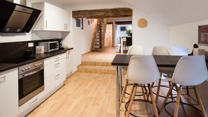 A modern kitchen with white cabinets, stainless steel appliances, and a wooden staircase leading to a dining area with a table and chairs. - Superb Duplex Ideally Located in the Centre of Aywaille (Aywaille)