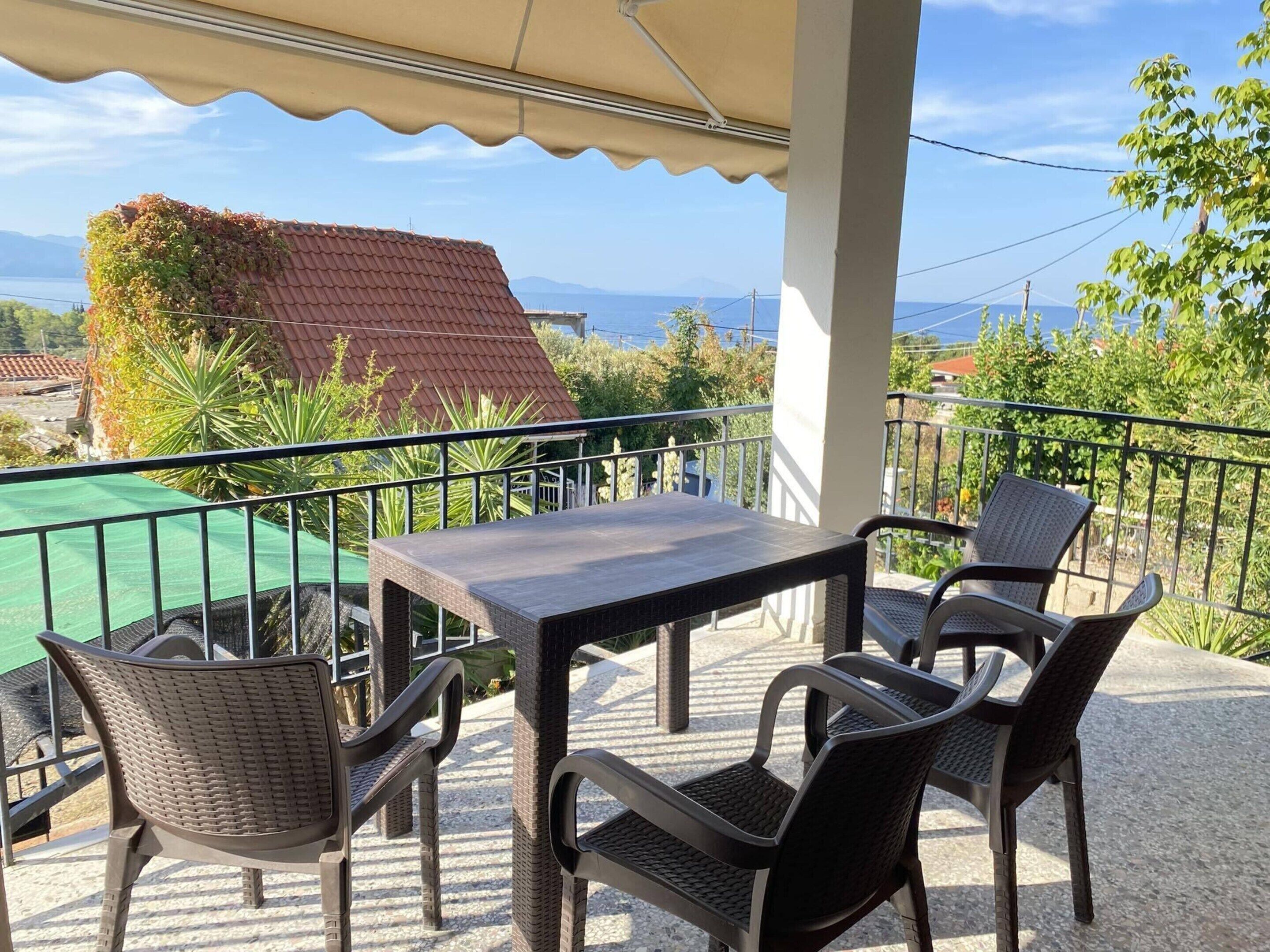 Un balcón con mesa y sillas, una sombrilla verde y vistas a casas y montañas.