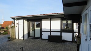 A building with a tiled roof, a sliding glass door, and a small outdoor seating area with a bench. - Vacation home Deichblüte in the vacation village Altes Land - Holiday home 39 Deichblüte 70sqm (Hollern-Twielenfleth)