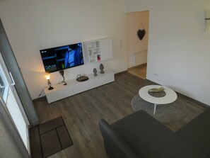 A modern living room with a flat-screen TV, a white entertainment unit, a round coffee table, and a grey sofa.