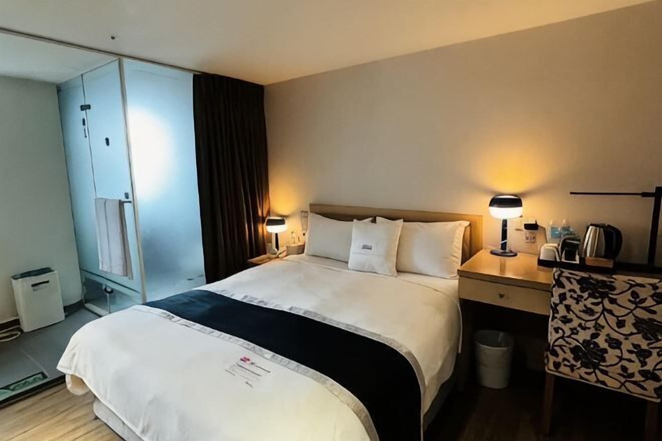 A hotel room with a bed, bedside tables, a lamp, a chair, and a wardrobe.