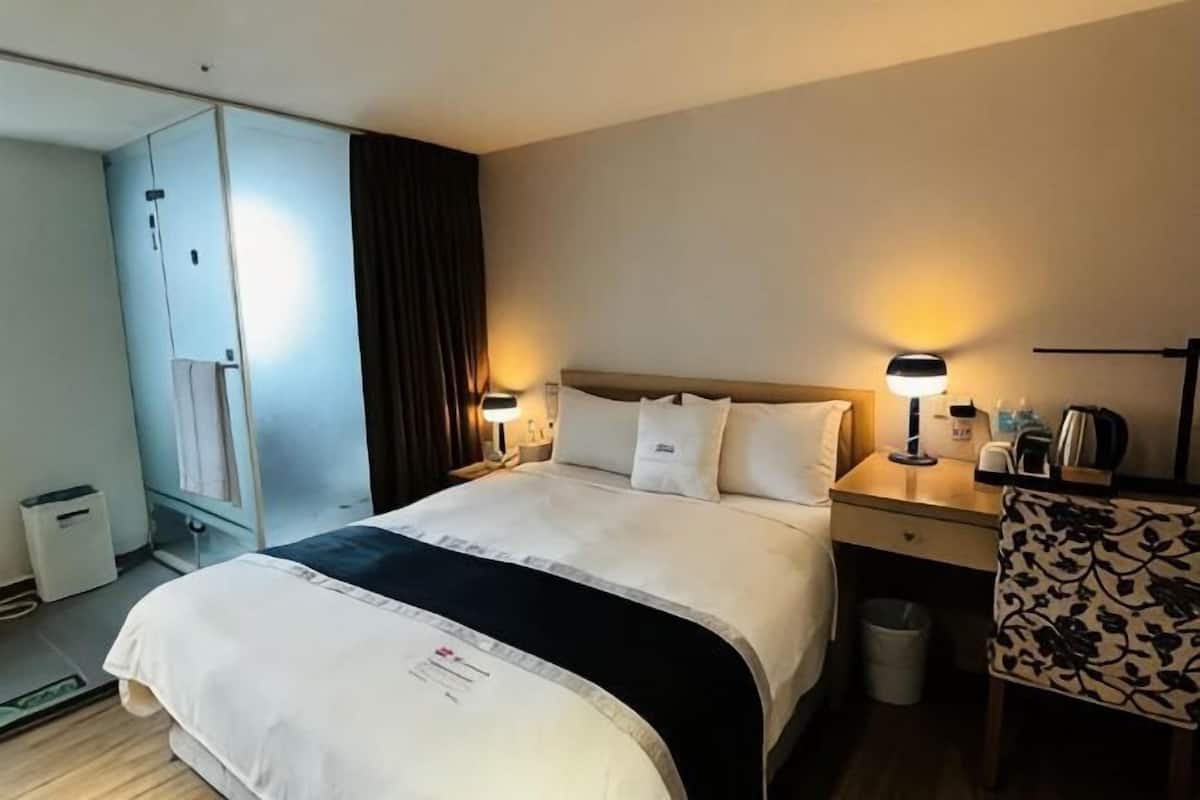 A hotel room with a bed, bedside tables, a lamp, a chair, and a wardrobe.