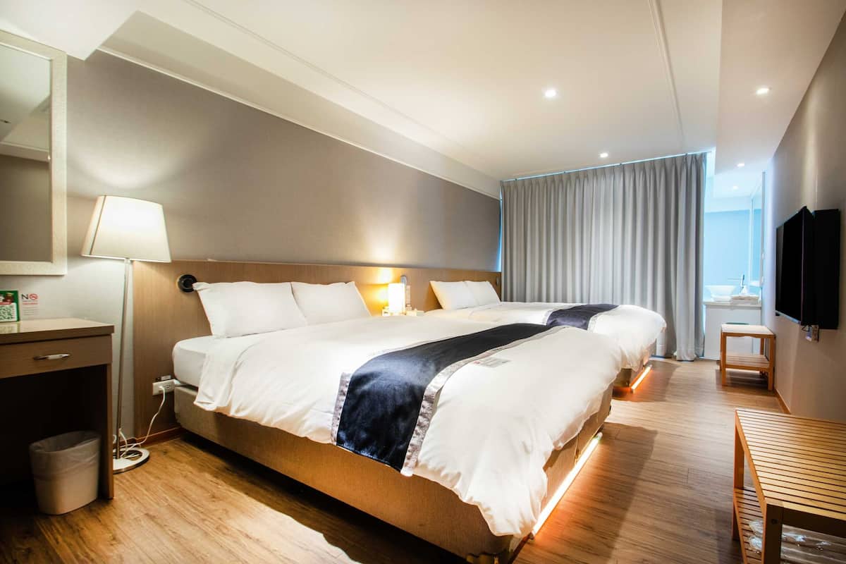 A hotel room with a large bed, bedside tables, a desk, a lamp, a TV, and a view of the outdoors.