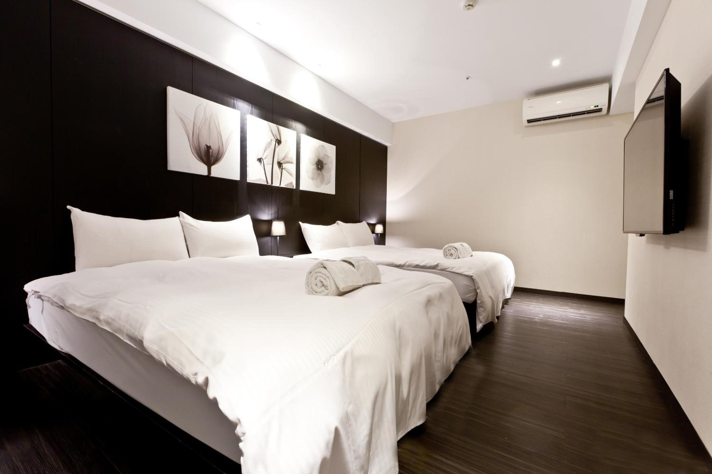 A hotel room with a large bed, a flat-screen TV, and an air conditioning unit.