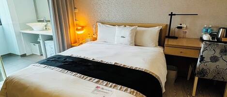 A hotel room with a bed, bedside table, lamp, and a desk with a chair.