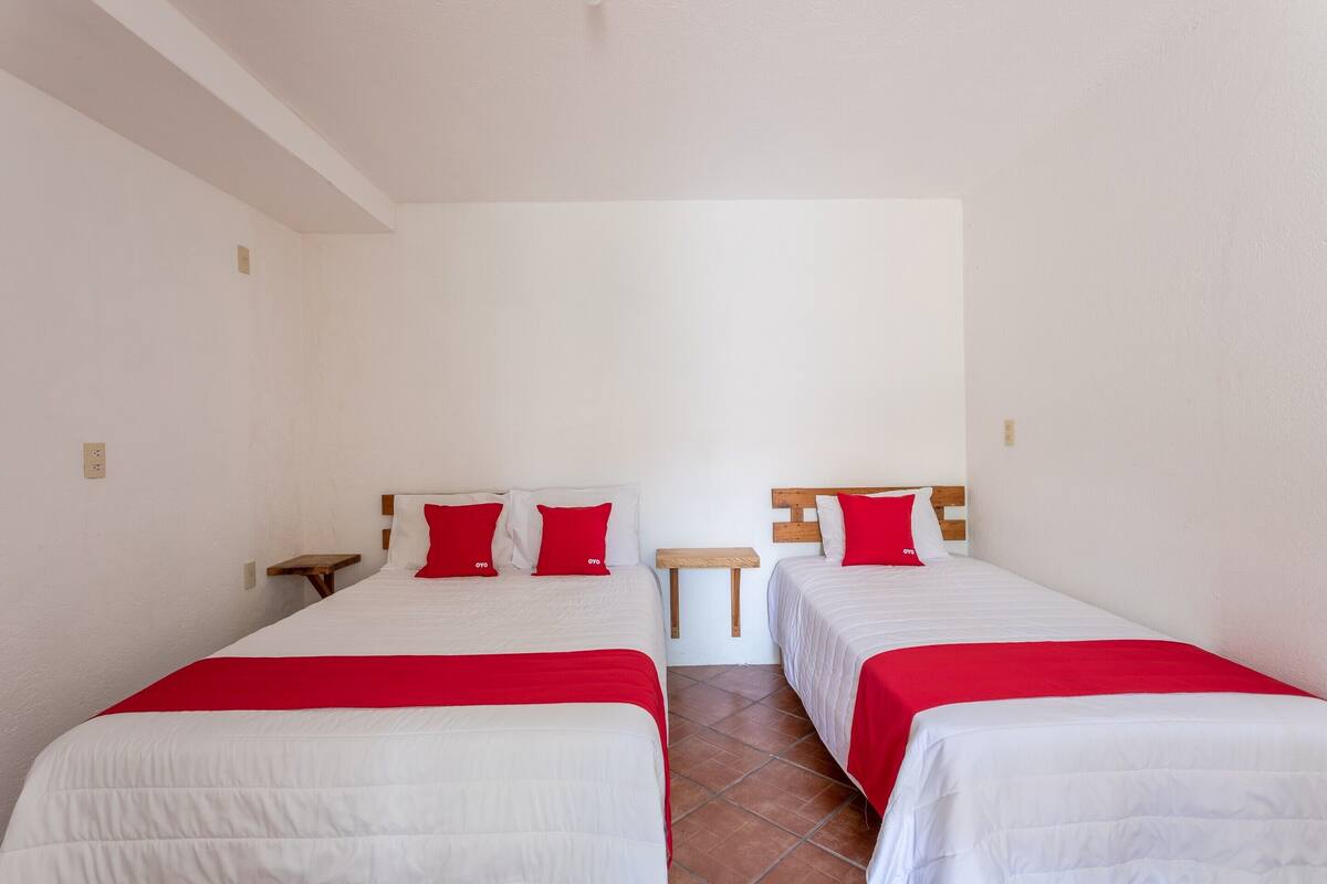 Une chambre d’hôtel avec deux lits, chacun recouvert d’une couverture rouge et blanche, et une petite table de chevet en bois placée entre les deux.
