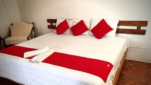 A neatly made bed with a white and red bedspread, a wooden headboard, and a chair in the corner. - Hotel Paraje Casa Blanca (San Agustin Etla)