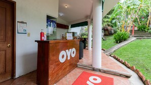 A reception desk with a sign reading "OYO" in a hotel lobby with a tiled floor, a green awning, and a small garden area with a pathway. - Hotel Paraje Casa Blanca (San Agustin Etla)
