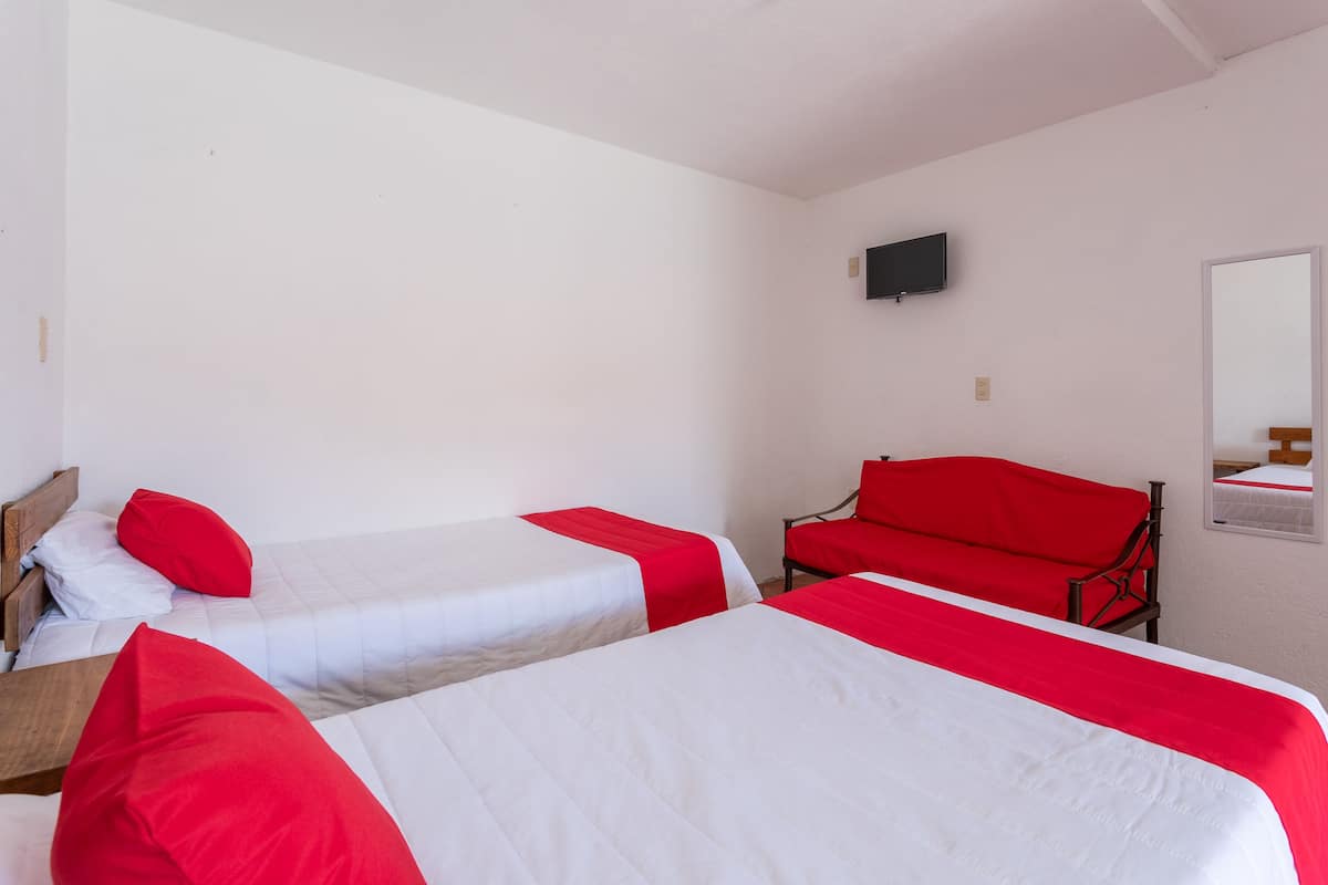 Une chambre avec deux lits, chacun agrémenté de draps rouges et blancs, un canapé rouge, un téléviseur fixé au mur et un miroir également fixé au mur.