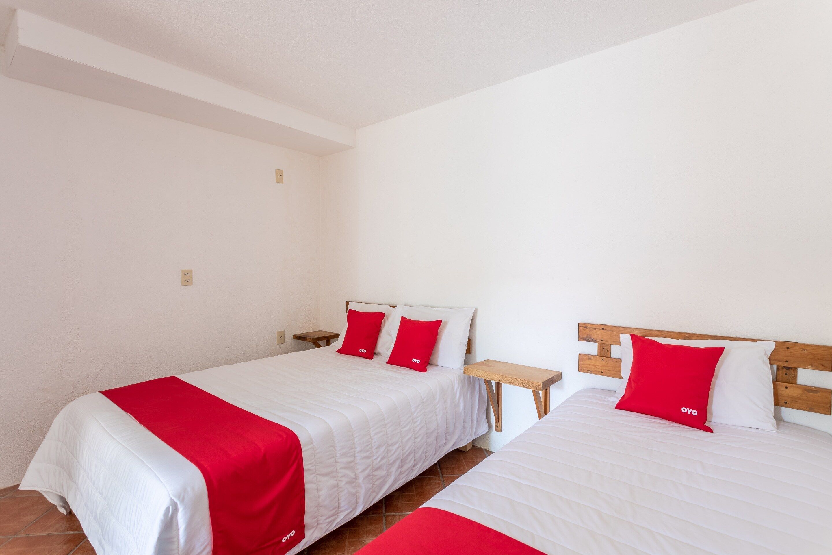 Two single beds with white and red bedding, wooden headboards, and a small bedside table.