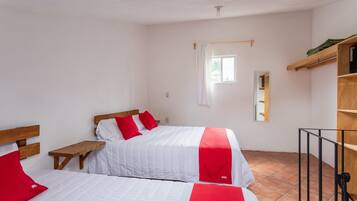 Una habitación con dos camas, cada una con ropa de cama roja y blanca, un banco de madera, una mesita pequeña y un estante de madera con un espejo.