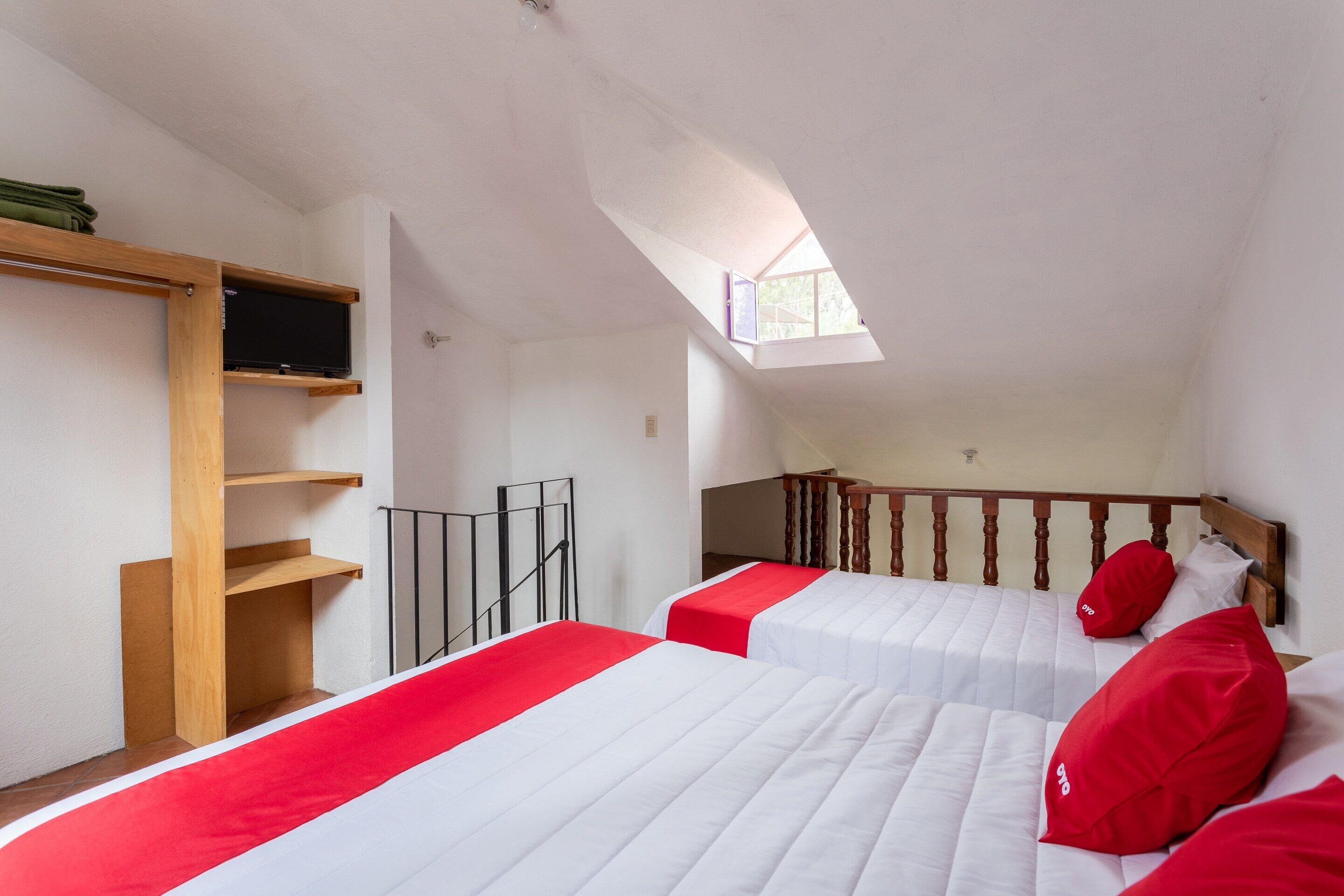 A bedroom with two beds, a wooden shelf, a TV, and a skylight.