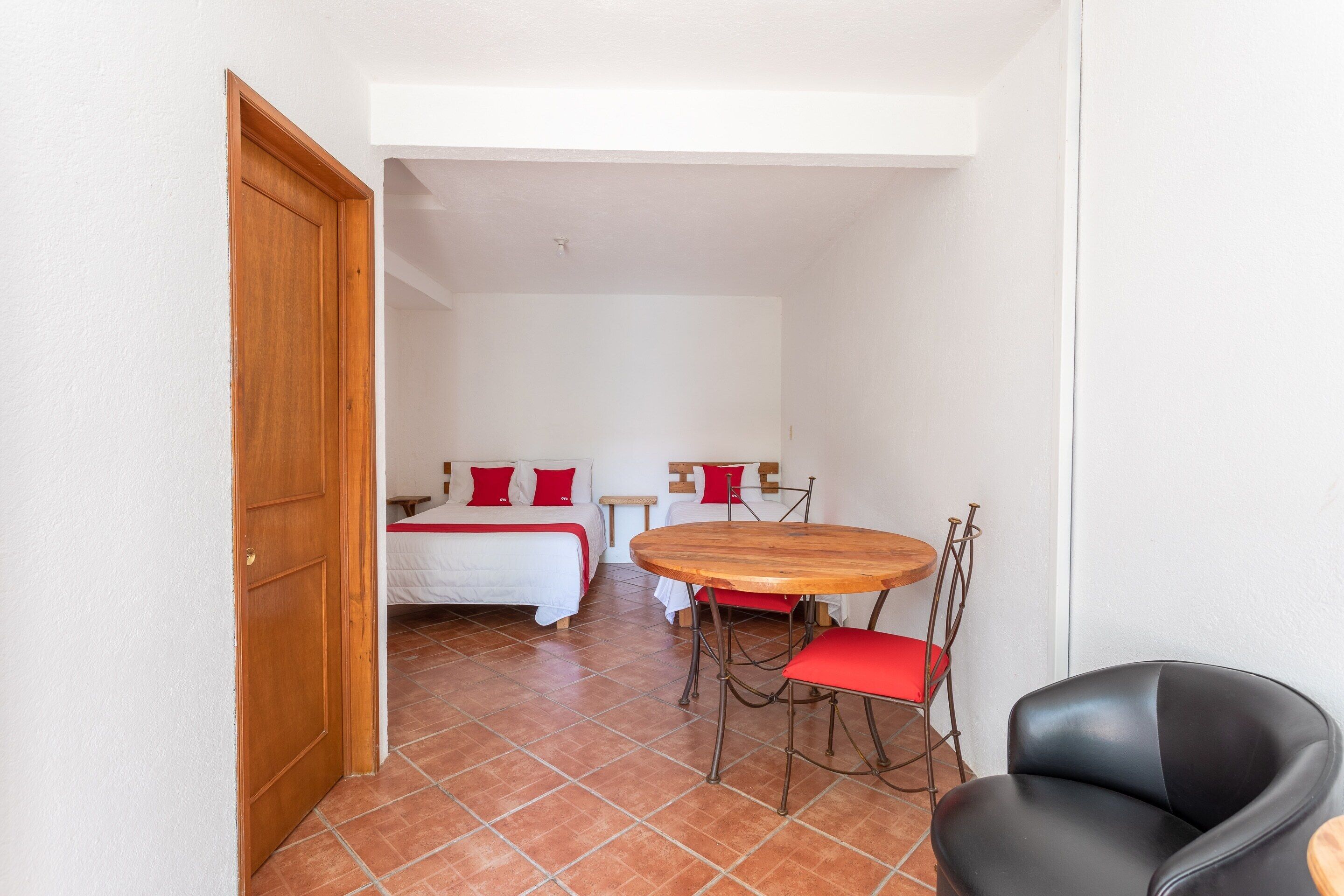 A room with a bed, a round wooden table with chairs, and a black leather chair.