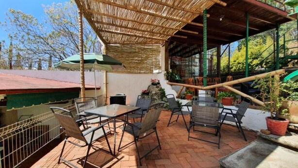 An outdoor patio with a bamboo roof, brick flooring, and metal chairs and tables. - Hotel Paraje Casa Blanca (San Agustin Etla)