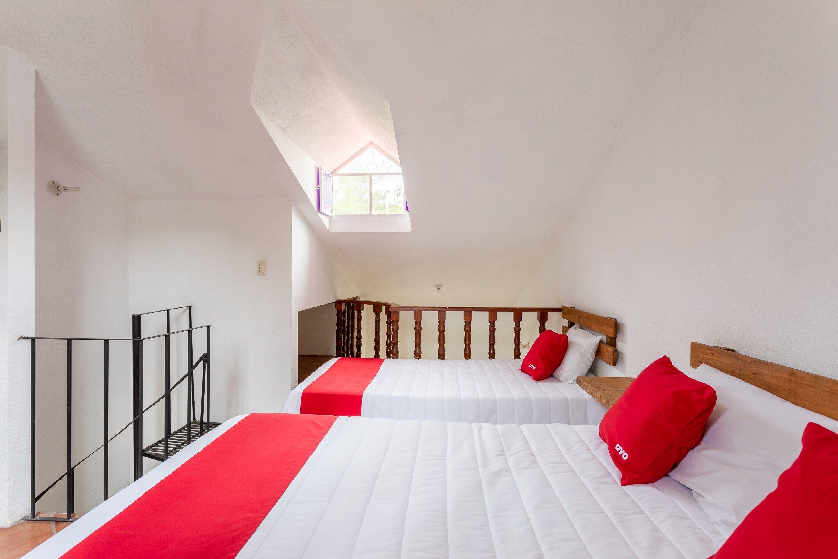 A bedroom with two beds, a wooden headboard, a red pillow, and a skylight.