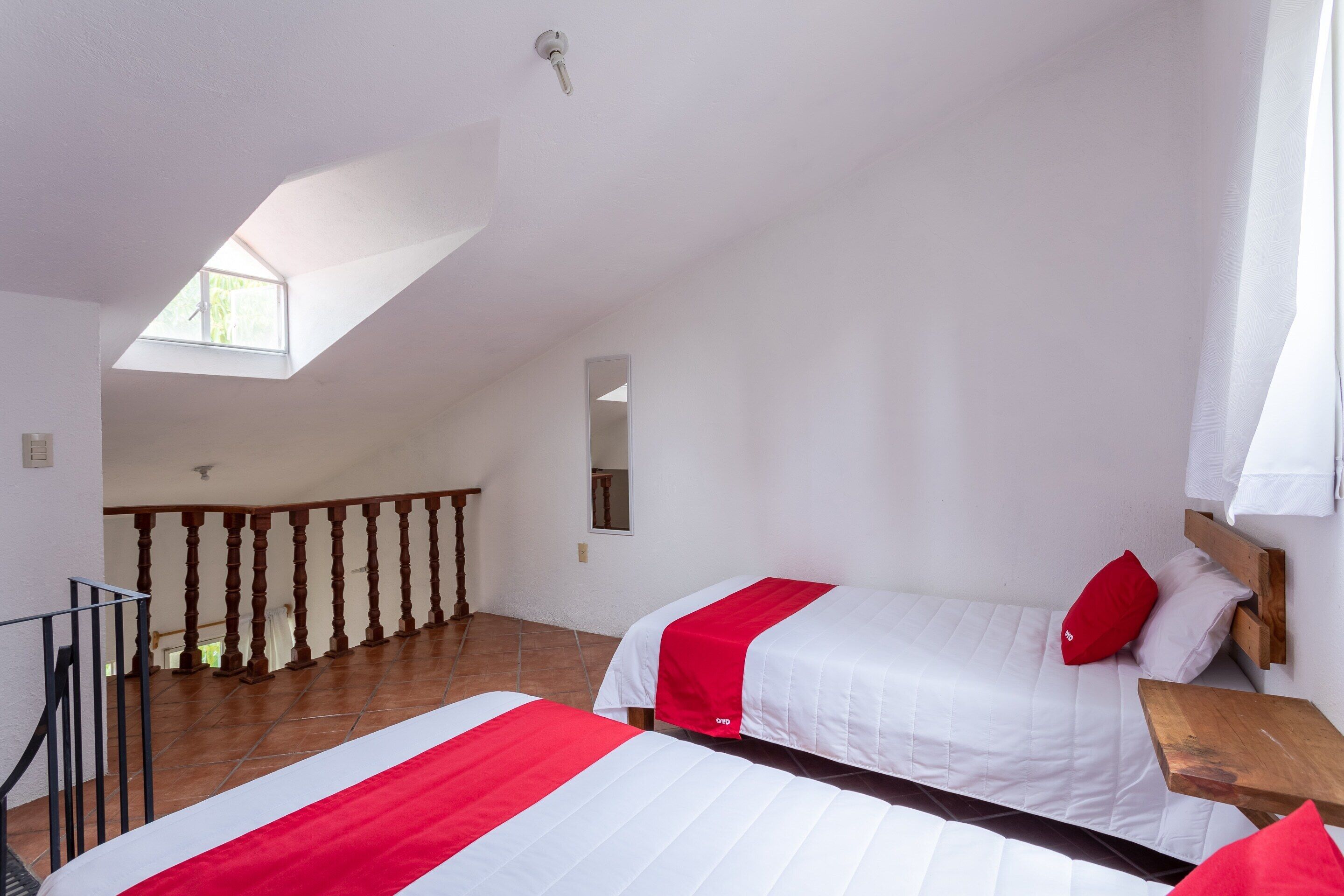 A bedroom with two beds, a wooden bench, a small table, a window, and a balcony.