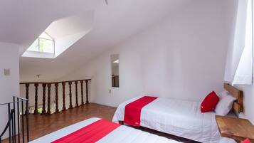 A bedroom with two beds, a wooden bench, a small table, a window, and a balcony.