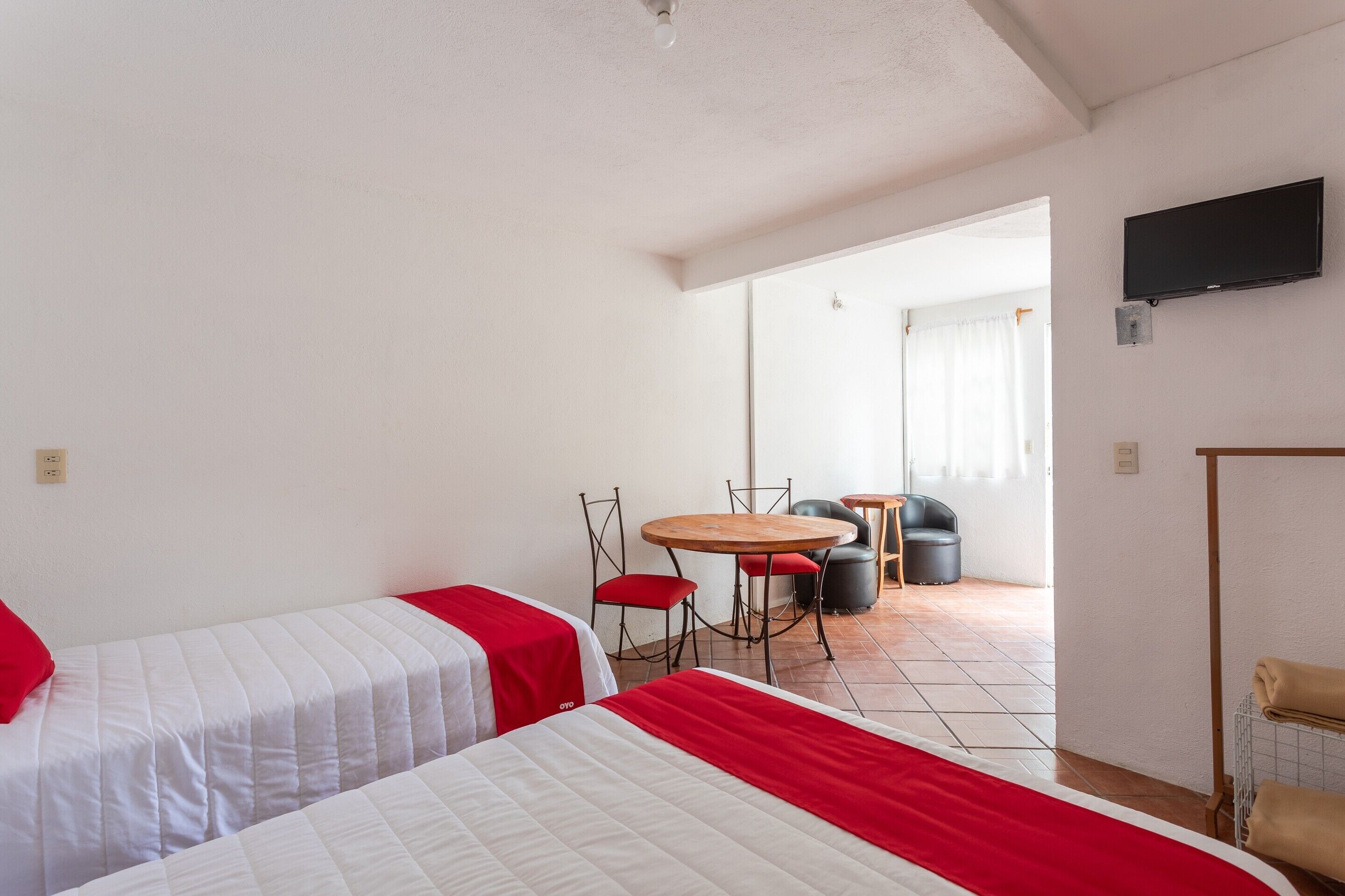 Habitación de hotel con dos camas, una mesita redonda con sillas, un televisor montado en la pared y un espejo grande que refleja la habitación.