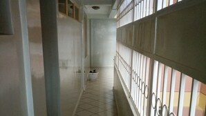 Un pasillo con piso de baldosas, una puerta blanca a la izquierda y una barandilla de metal a la derecha.