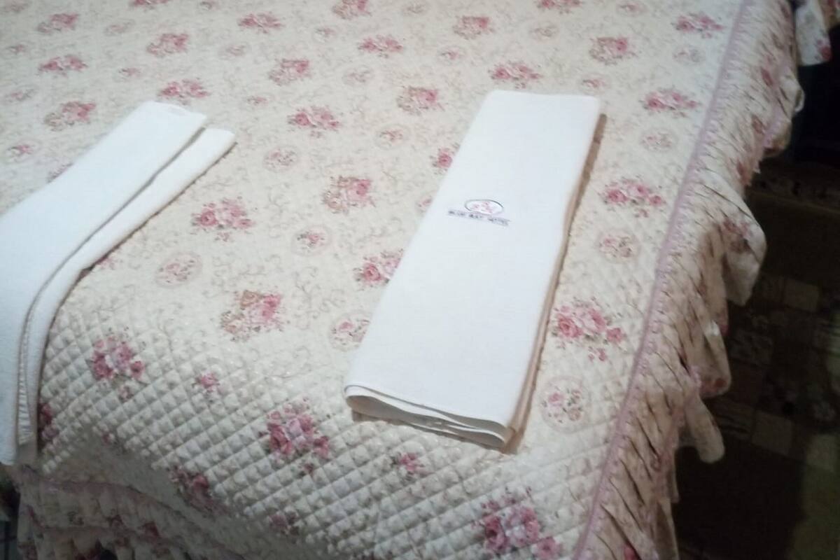 A bed with a floral bedspread, a neatly folded white towel, and a white blanket.