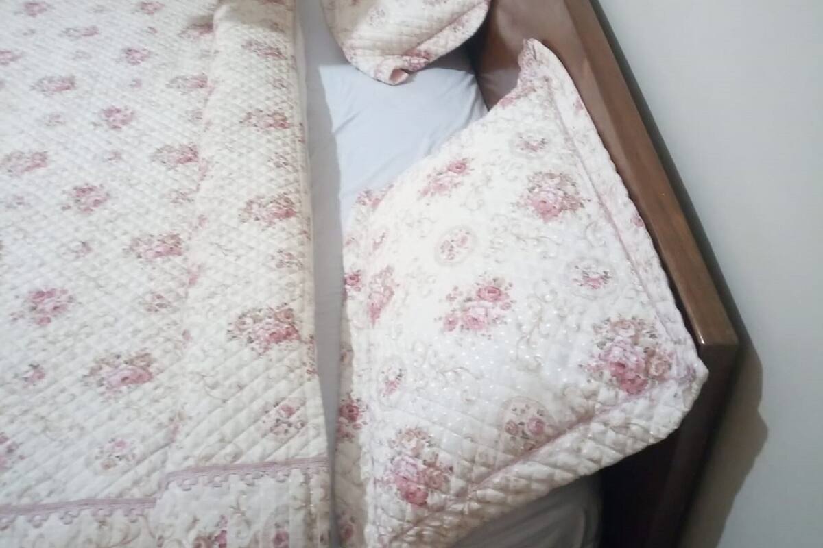 A bed with a floral patterned bedspread and pillows, a wooden headboard, and a plain wall in the background.