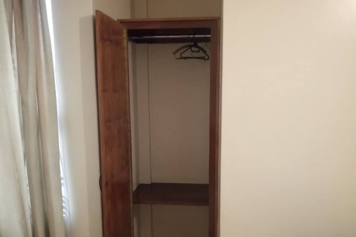 A room with a wooden wardrobe, a tiled floor, and a television on a wooden stand.
