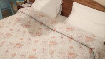 A bed with a floral-patterned bedspread and white pillows, a wooden headboard, and a nightstand with a lamp.