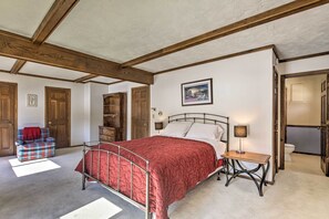 A bedroom with a large bed, a wooden chair, a small table, and a door leading to another room. - Simple Cranberry & Wine Farm Home w/ Fire Pit! (Eagle River)