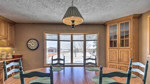 A dining area with a wooden table and chairs, a hanging light fixture, and a large window with a view of the outside. - Simple Cranberry & Wine Farm Home w/ Fire Pit! (Eagle River)