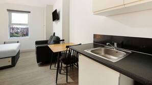 A compact kitchen with a dining area, a sofa, and a TV mounted on the wall. - Modern Studio in London Near Wimbledon Park (London)