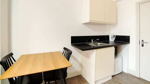 A small kitchen with a black countertop, a sink, and a white cabinet. There is a wooden table with four chairs. - Modern Studio in London Near Wimbledon Park (London)
