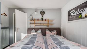 A bedroom with two beds, a wardrobe, a shelf with decorative items, and a wall with a 'Relax' sign.