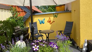 An outdoor patio with a yellow wall, a table, two chairs, a statue, and decorative butterflies.