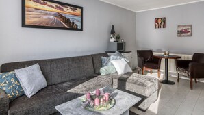 A modern living room with a grey sofa, a coffee table with candles, a painting of a sunset, and a dining area with a table and chairs. - Bungalow in Wernigerode (Wernigerode)