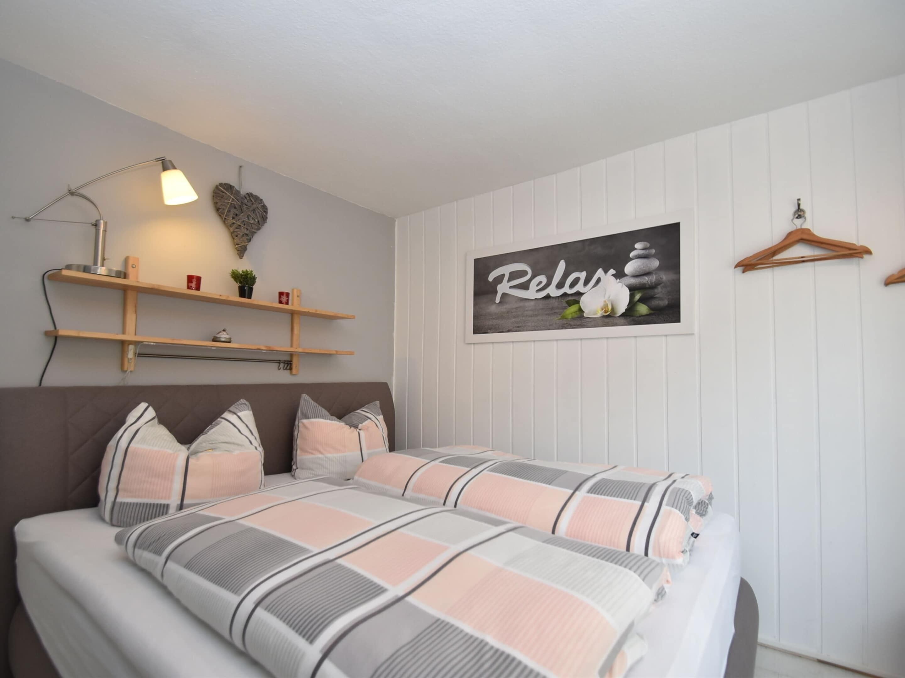 Een slaapkamer met een bed, een wandplank met decoratieve items, een kunstwerk aan de muur en een houten kapstok.
