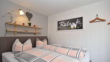 Een slaapkamer met een bed, een wandplank met decoratieve items, een kunstwerk aan de muur en een houten kapstok.
