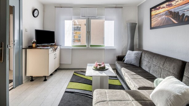 A modern living room with a sofa, a coffee table, a TV, and a window with blinds. - Bungalow in Wernigerode (Wernigerode)