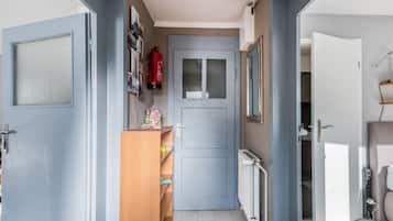 Een smalle gang met een grijze deur, een klein houten kastje en een radiator aan de rechterkant.