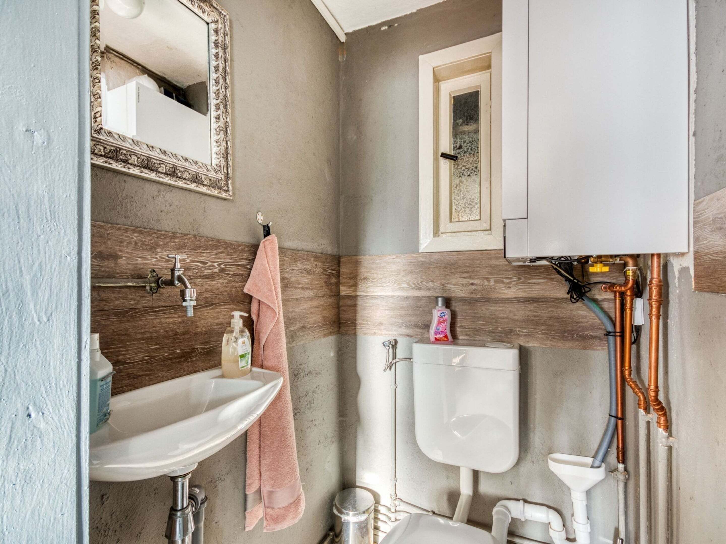 A bathroom with a sink, mirror, toilet, and visible plumbing.